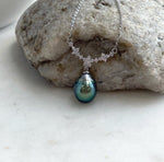 Tahitian pearl necklace displayed against a cream stand, showing its green pearl and sparkling floral centerpiece.