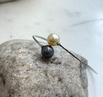 Two-tone ocean pearl bangle displayed on a pale surface beside natural driftwood.