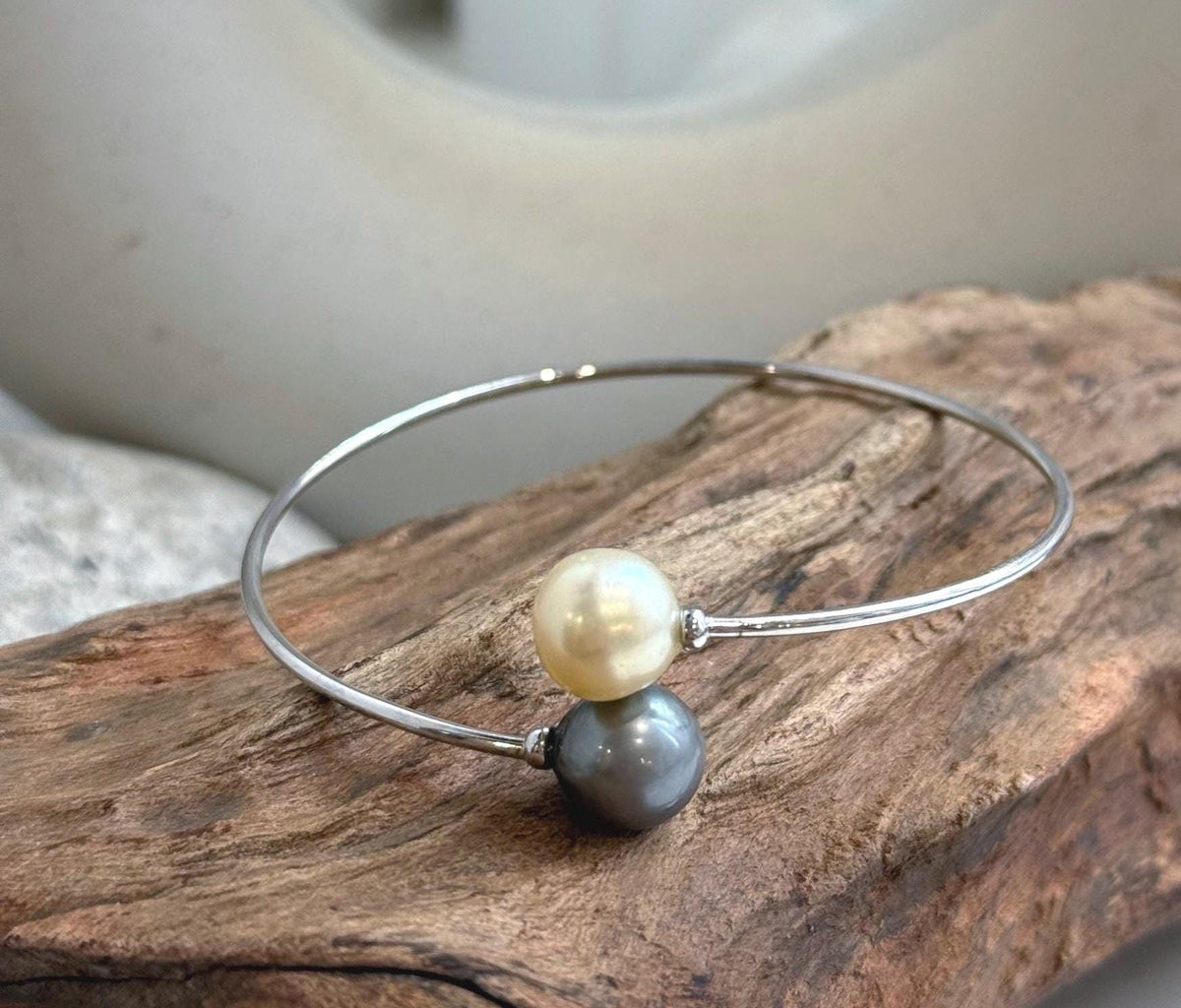 Champagne gold and platinum gray pearls meet at the opening of a silver bangle.