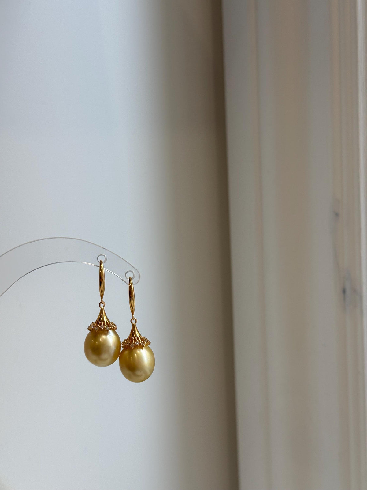 Golden South Sea pearl earrings with flared crystal-accented caps and curved hooks.