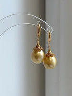 Golden pearl hook earrings with sparkling accents around the pearl caps.