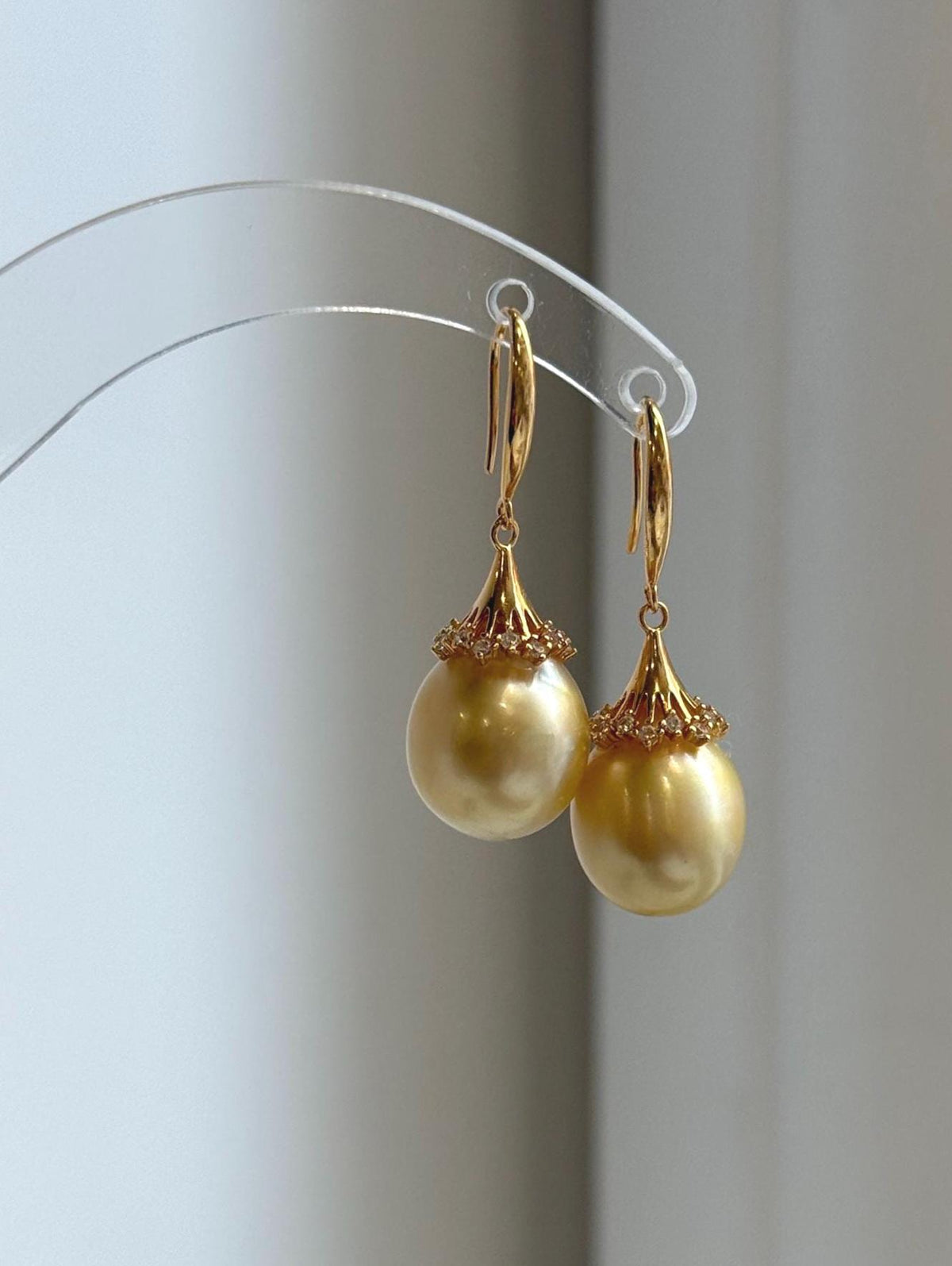 Golden pearl hook earrings with sparkling accents around the pearl caps.