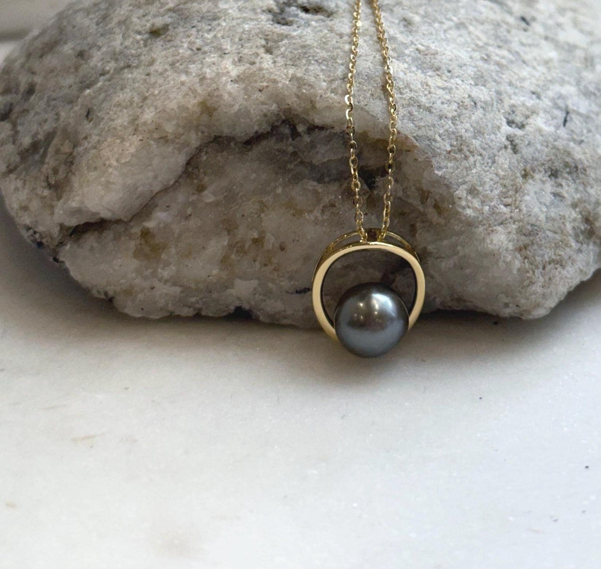 Lustrous taupe platinum pearl nestled at the base of an open gold-tone circle.