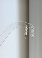 Triple pearl hook earrings with polished silver tips extending below the pearls.