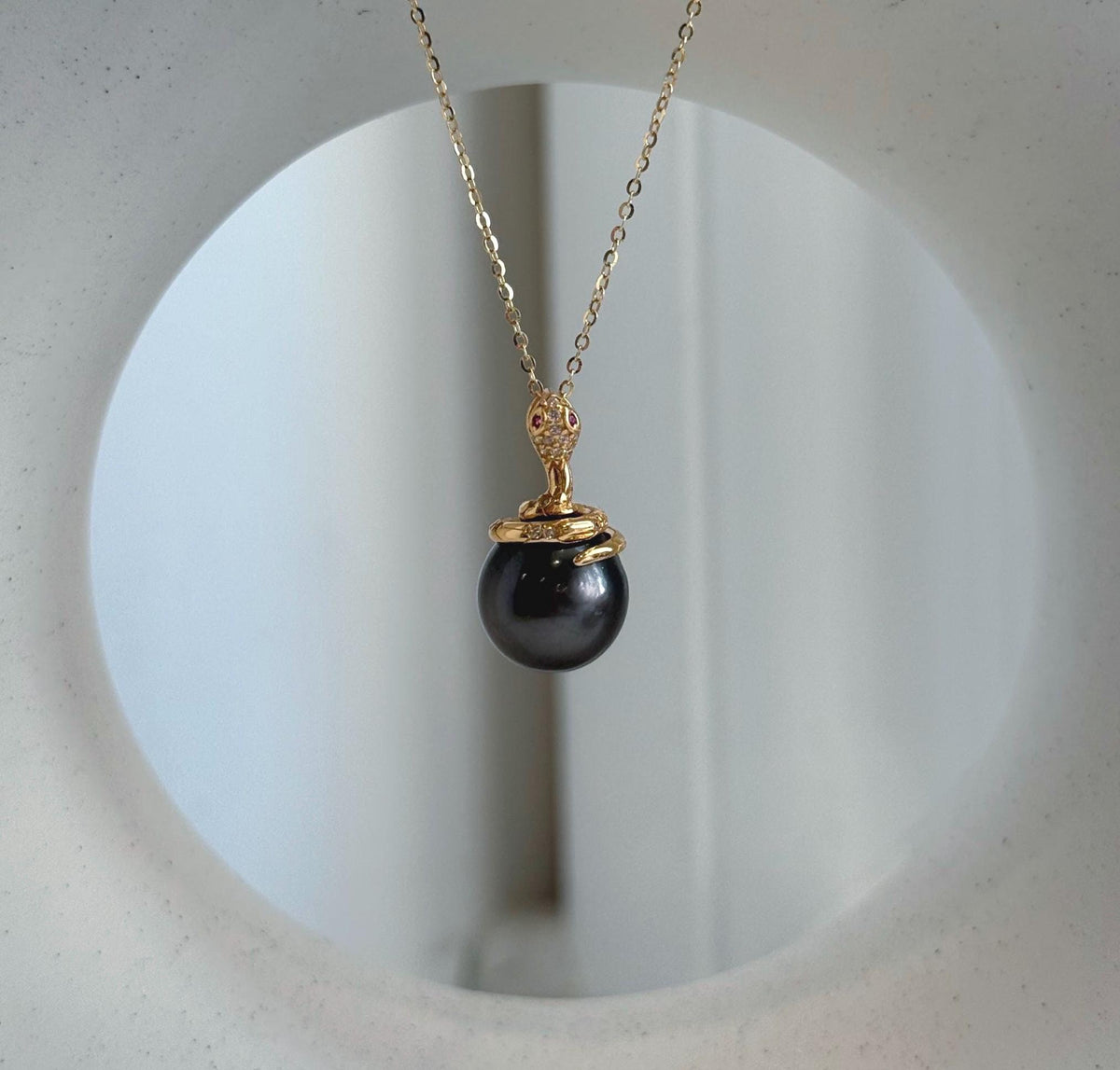 Close view of a reflective piano black pearl with a gold-tone serpent curling around its upper edge.
