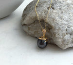 Tahitian pearl snake necklace laid flat beside its handwritten product label.