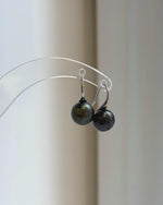 Dark green pearl earrings hanging from a clear acrylic display.