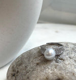 Australian white pearl ring resting beside a branch on a ceramic vase.