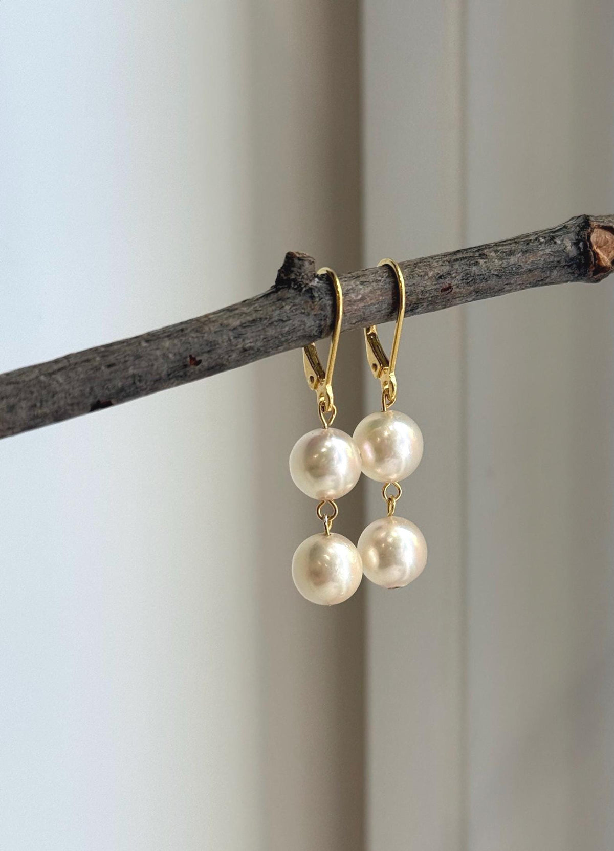 Ivory Akoya pearl earrings resting beside a clear bag with handwritten measurements.