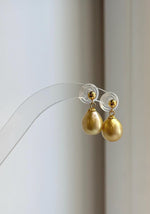 Golden South Sea pearl earrings displayed on a clear stand.