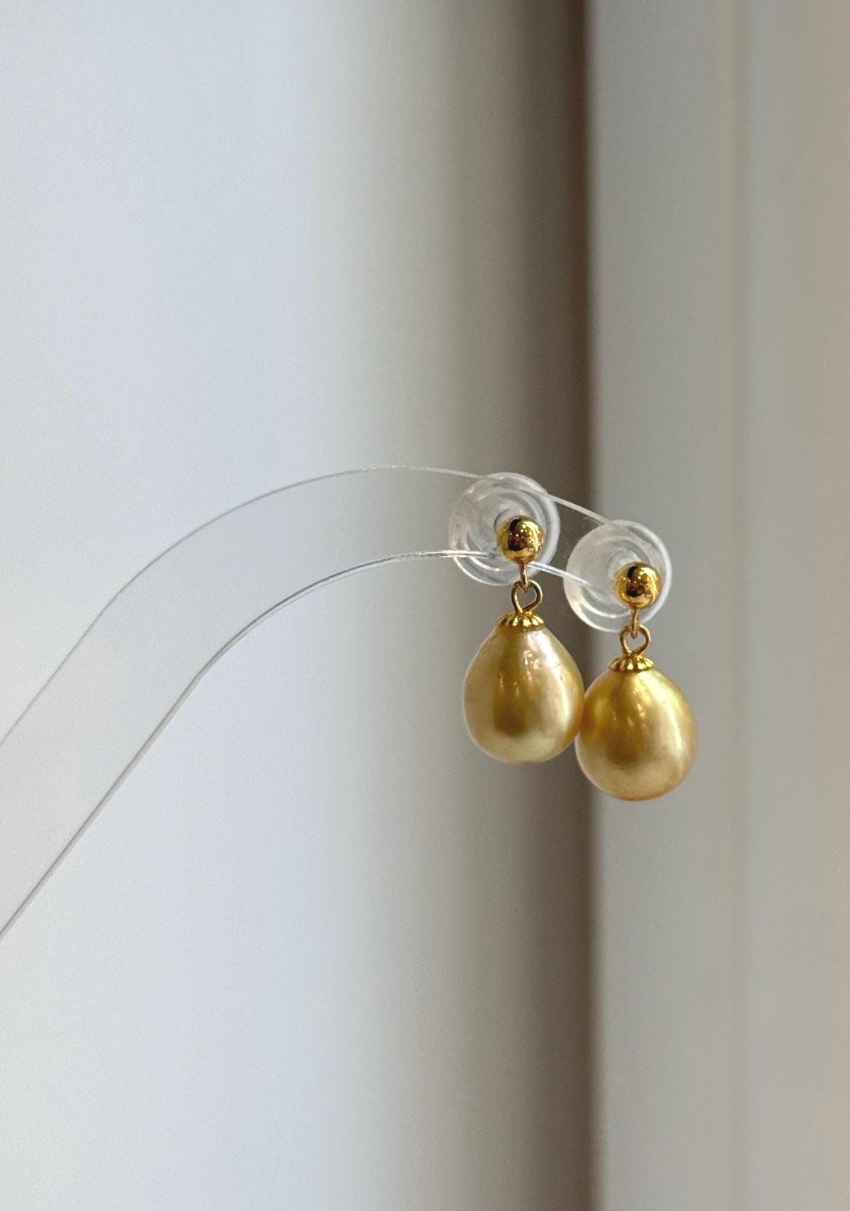 Golden South Sea pearl earrings displayed on a clear stand.