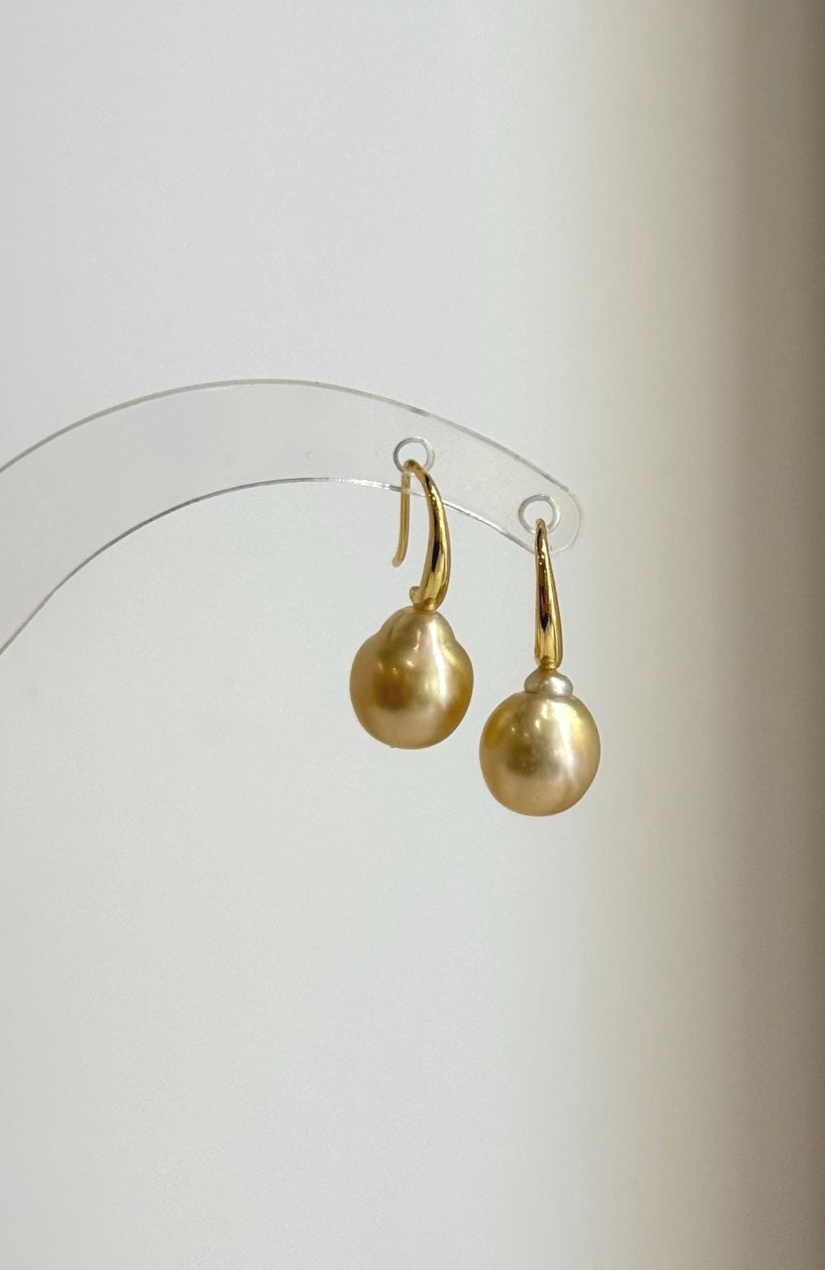 Golden saltwater pearls suspended from curved sterling silver ear hooks.