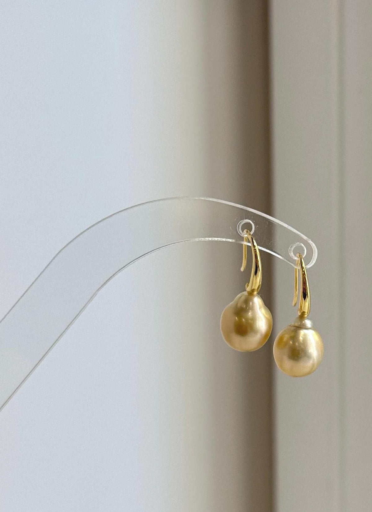 Golden saltwater pearls suspended from curved sterling silver ear hooks.