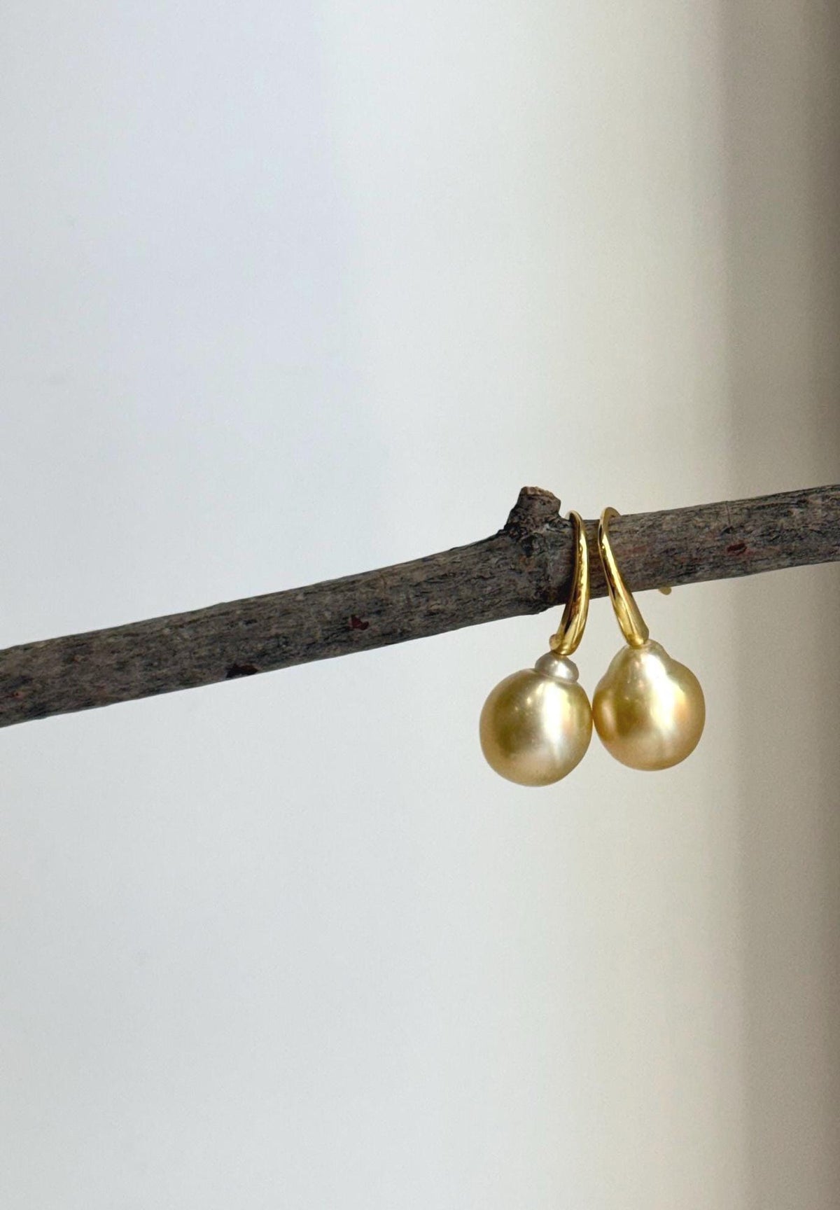 Golden pearl earrings displayed against a soft neutral background.