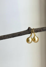 Golden pearl earrings displayed against a soft neutral background.