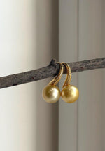 Golden pearl drop earrings with distinctive high-heel style hooks.