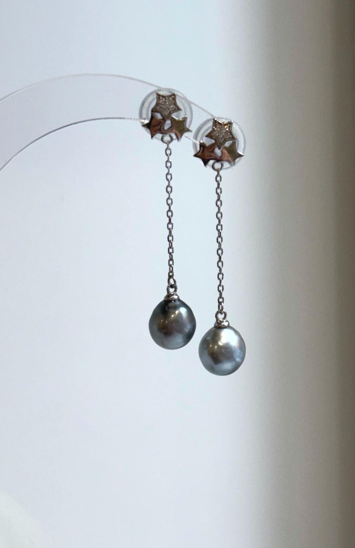 Tahitian pearl star earrings displayed on a clear stand