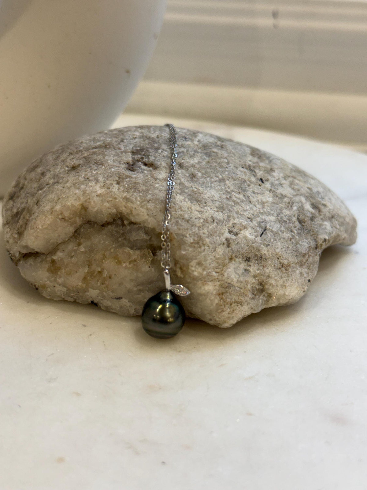Tahitian pearl necklace displayed against a cream stand, showing its dark green color and reflective luster.