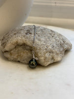 Tahitian pearl necklace displayed against a cream stand, showing its dark green color and reflective luster.