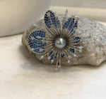 Gray pearl flower brooch with blue and clear sparkling accents in a silver-tone setting.