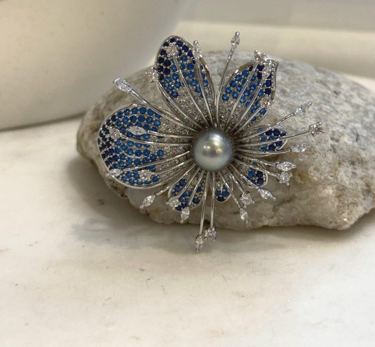 Gray pearl flower brooch with blue and clear sparkling accents in a silver-tone setting.