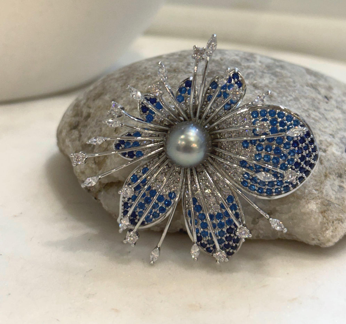 Sculptural floral brooch featuring a lustrous gray pearl at its center.