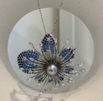 Flower-shaped brooch with deep blue accents and a reflective gray pearl.