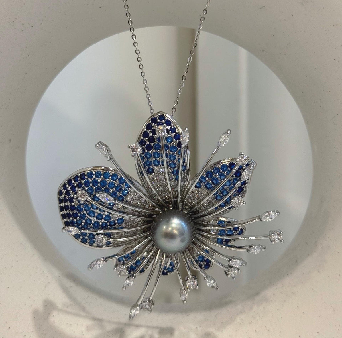 Flower-shaped brooch with deep blue accents and a reflective gray pearl.
