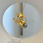Two elephants with curled trunks and polished gold-tone ears beside a dark Tahitian pearl.