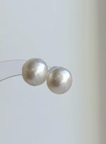 White saltwater pearl studs featuring reflective surfaces and sterling silver settings.