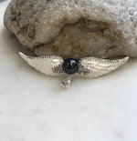 Black hunter green Tahitian pearl centered between silver-tone angel wings with a clear dangling accent.