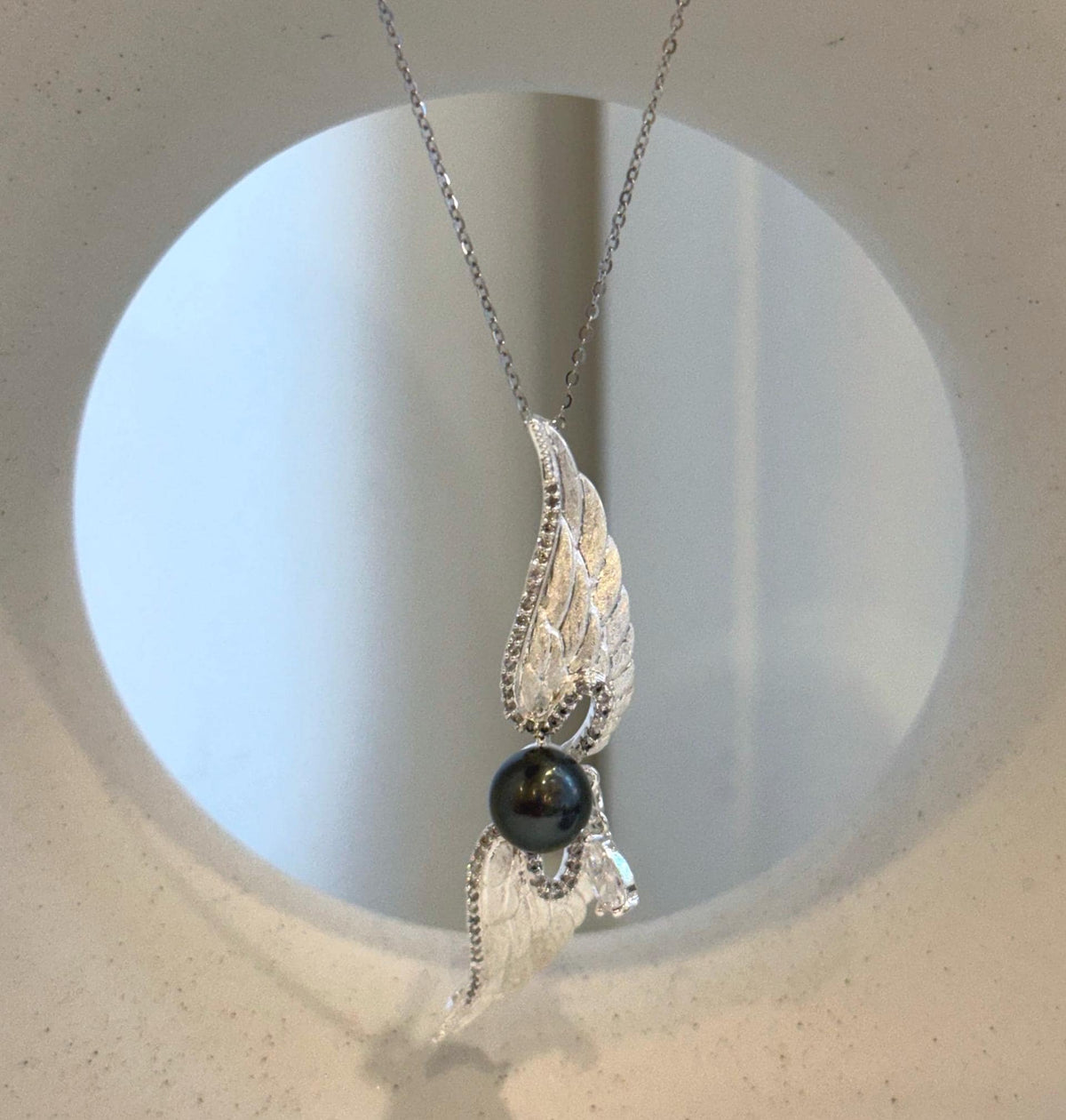 Dark Tahitian pearl framed by outstretched silver-tone wings and a sparkling drop.