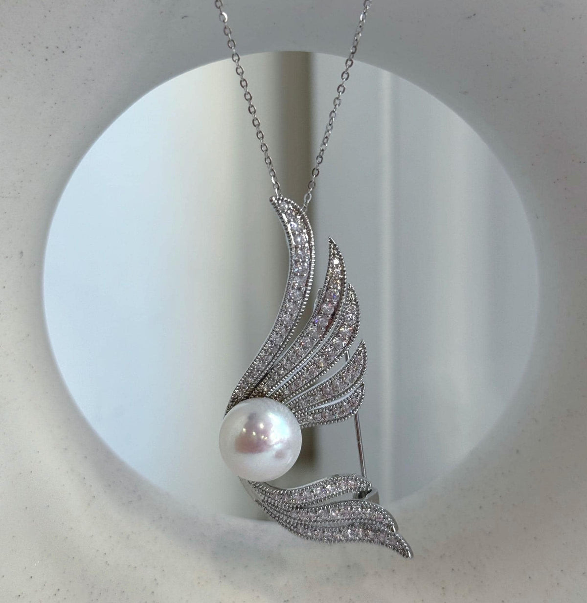 Lustrous white freshwater pearl framed by curved feather-inspired wings.