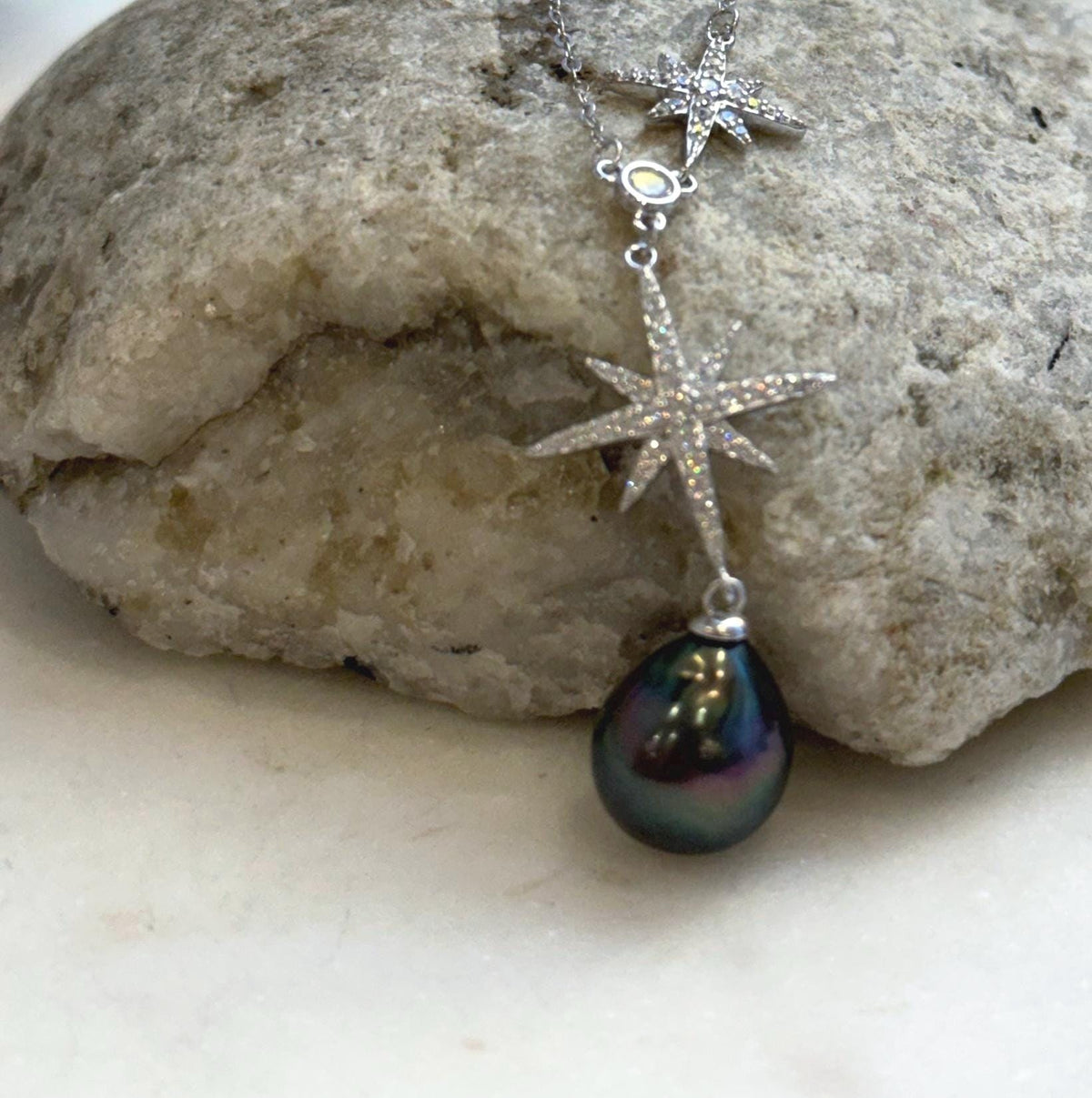 Teardrop Tahitian pearl displaying green and purple overtones beneath a silver starburst pendant.