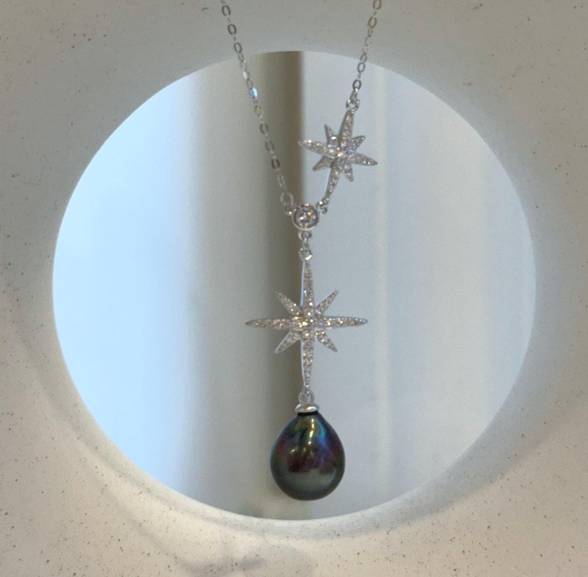 Sterling silver necklace featuring an asymmetrical star detail and a dark pearl drop.
