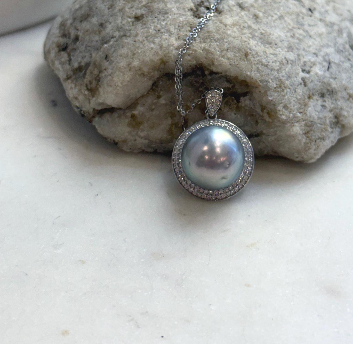 Lustrous Tahitian pearl framed by clear stones and suspended from a delicate silver chain.