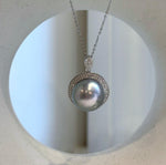 Silver-blue pearl pendant displayed against a cream ceramic vase with a circular opening.
