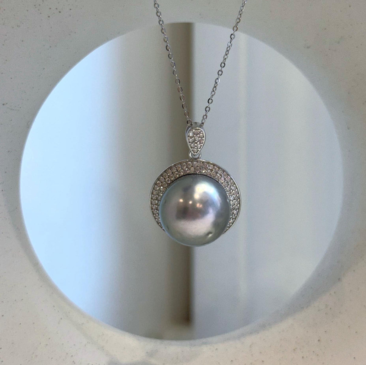Silver-blue pearl pendant displayed against a cream ceramic vase with a circular opening.