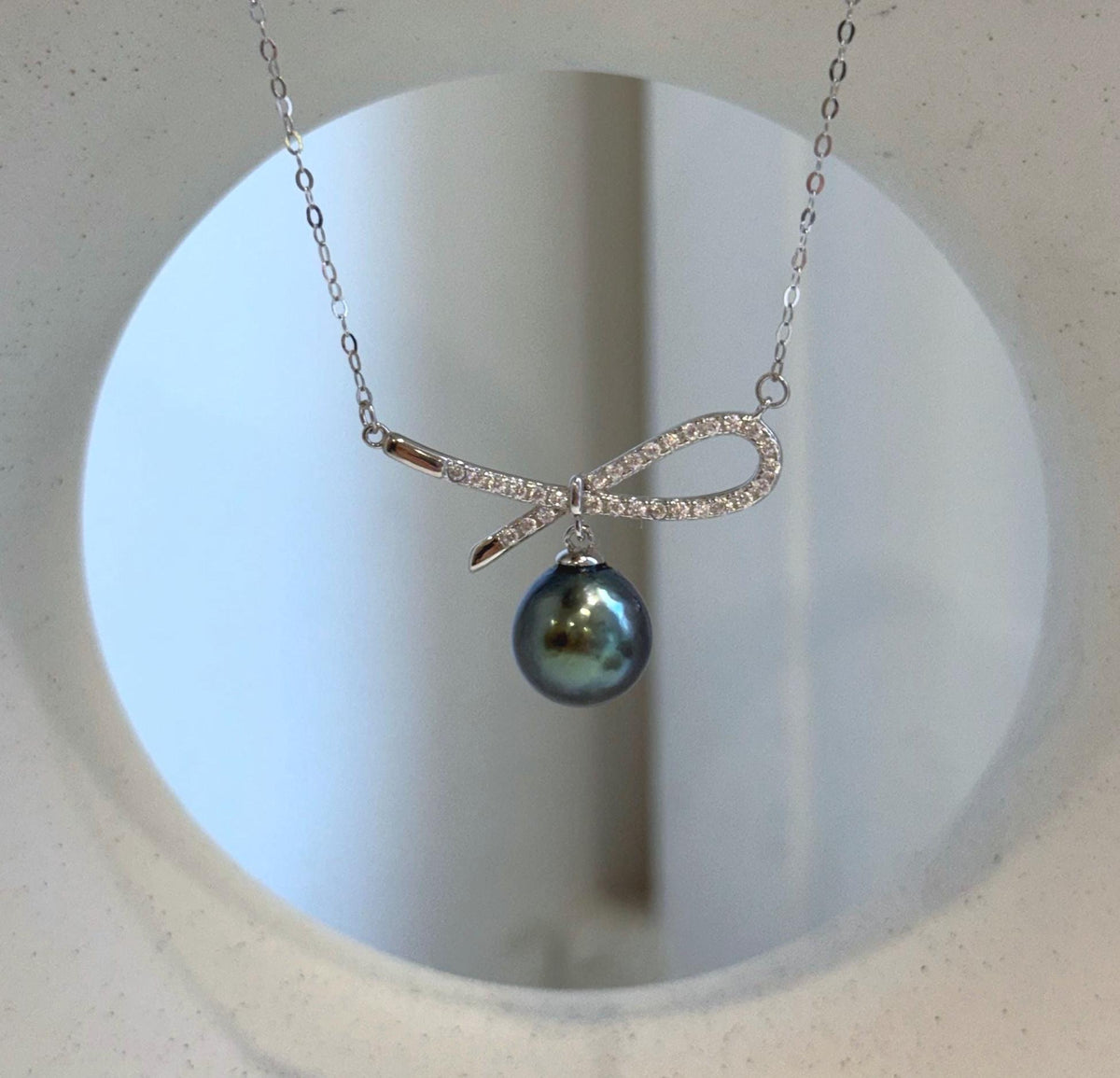 Tahitian pearl bow necklace displayed on a cream sculptural jewelry stand.