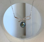 Tahitian pearl bow necklace displayed on a cream sculptural jewelry stand.