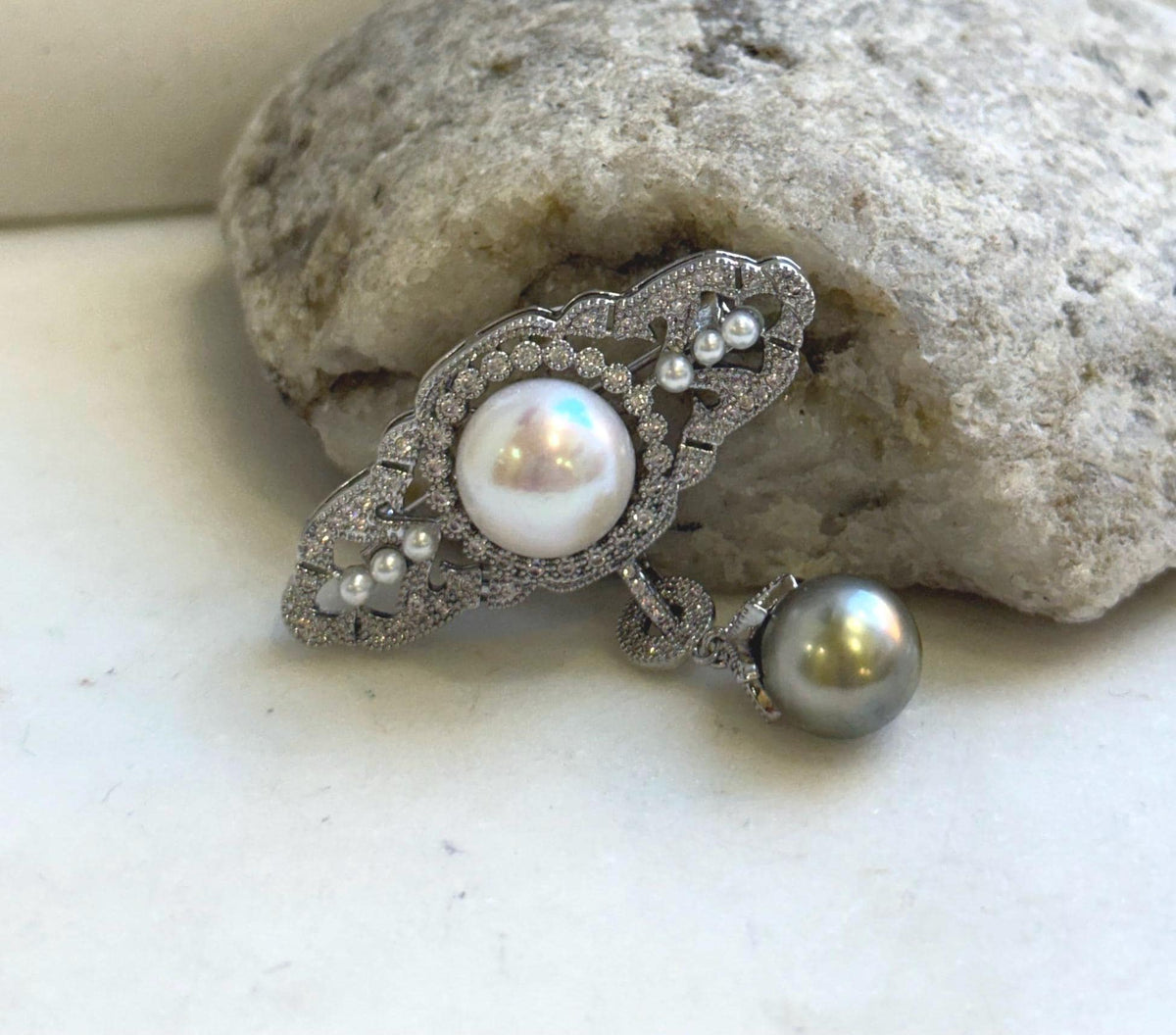 Pearl pendant brooch featuring a round white pearl and dangling dark pearl