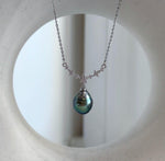 Dark Tahitian pearl with reflective teal and green tones beneath a delicate flower-accented silver setting.