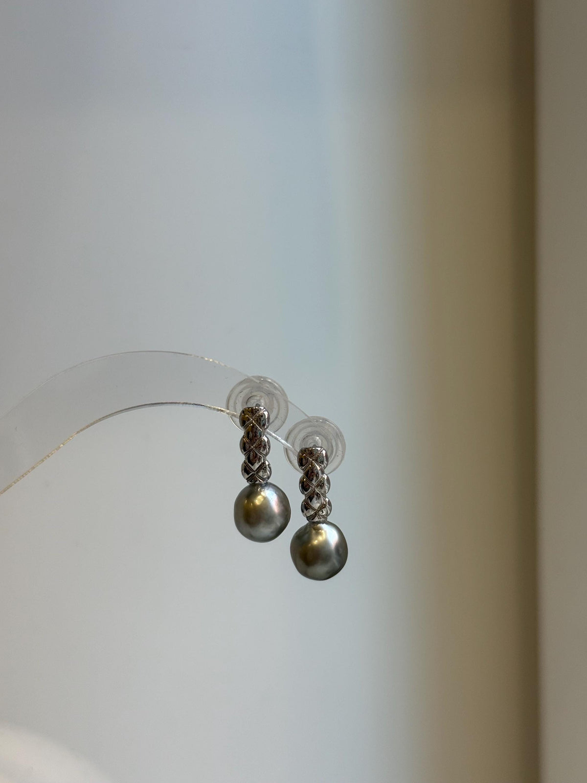 Pair of 9mm gray pearl earrings hanging from a transparent display against a softly lit cream background.