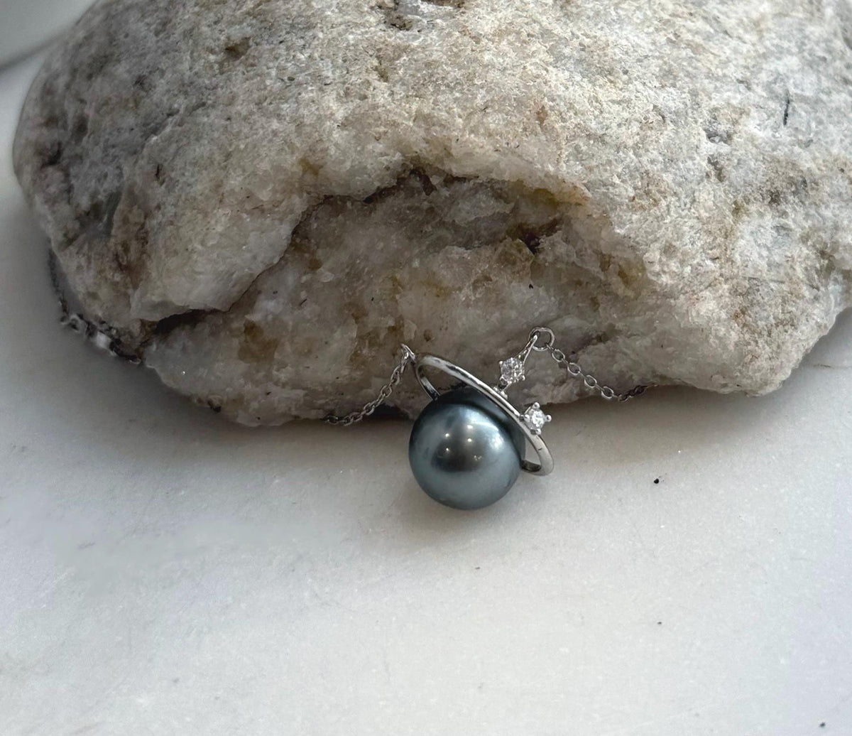 Tahitian pearl necklace displayed against a cream circular cutout stand, showing its silver orbit ring.