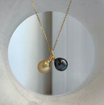 Golden South Sea and dark Tahitian pearl necklace displayed on a cream bust, with two pearls hanging side by side from a gold-tone pendant.
