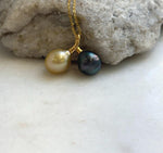 Golden South Sea and Tahitian pearl pendant with a curved gold-tone setting, hanging at the center of a fine chain on a necklace stand.