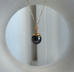 Dark Tahitian pearl pendant suspended from a delicate gold-tone chain against a white background.
