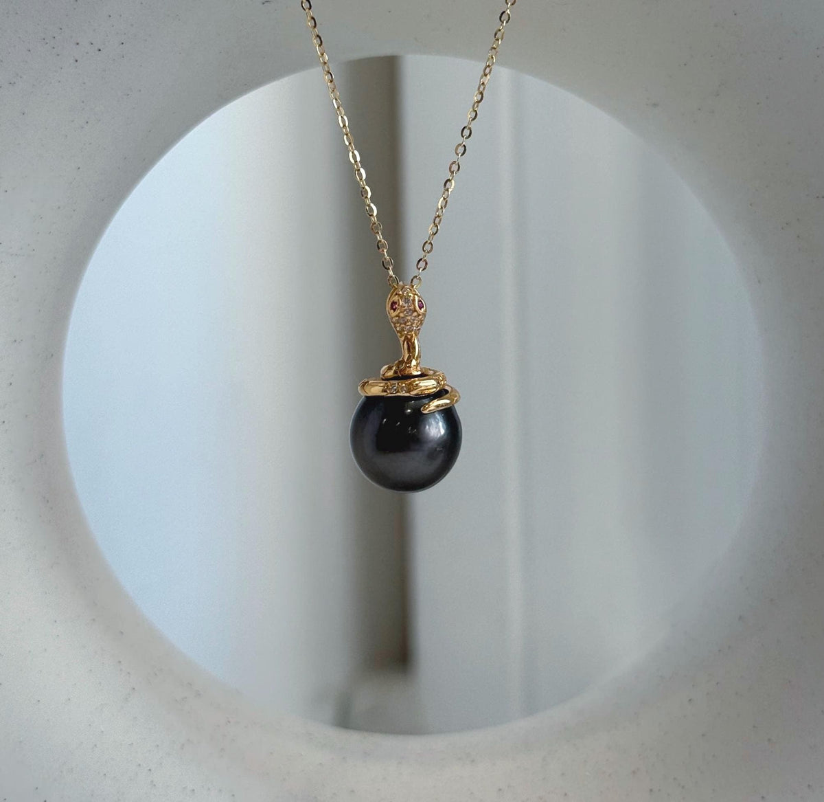 Dark Tahitian pearl pendant suspended from a delicate gold-tone chain against a white background.