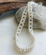 White pearl necklace draped over a natural stone beside driftwood.
