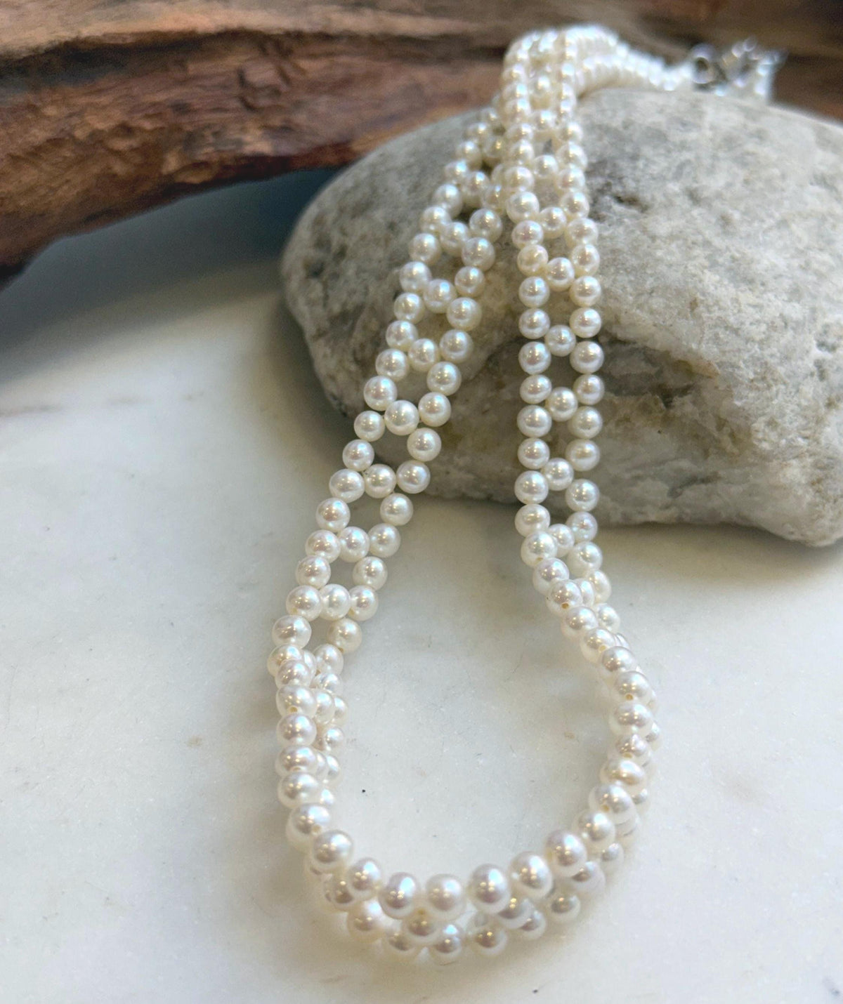 White pearl necklace draped over a natural stone beside driftwood.
